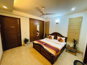 A bedroom with a bed, wardrobe, ceiling fan, bedside table, and a potted plant. - Fortune Home Service Apartment 4BHK J191 (New Delhi)