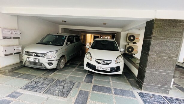 Zwei geparkte Autos in einer überdachten Parkgarage mit gefliestem Boden und einer Wand-Klimaanlage.