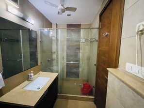 A bathroom with a glass-enclosed shower, a sink with a mirror, and a ceiling fan. - Fortune Home Service Apartment 4BHK J191 (New Delhi)