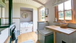 Een kleine kamer met een bed, een bankje, een wastafel en een raam met uitzicht op groen.
