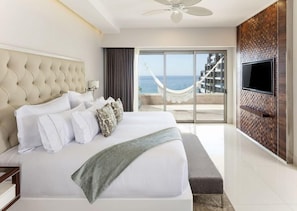 A modern hotel room with a large bed, a television, and a view of the ocean.