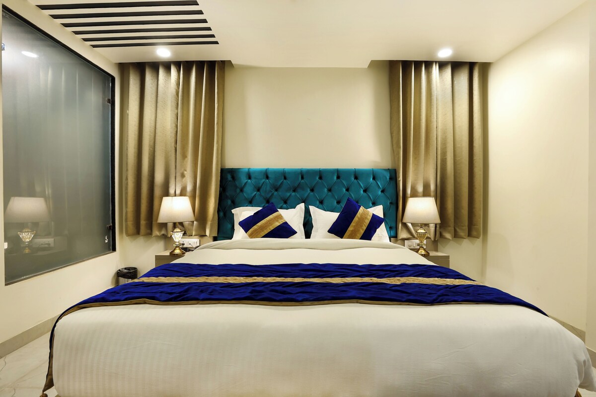 A hotel room with a large bed, two bedside tables with lamps, a tufted headboard, and curtains on the windows.
