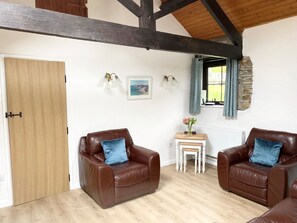 A room with two leather armchairs, a small wooden table, a framed picture, and a stone wall. - Shipload Cottage by Interhome (Bideford)