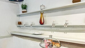 Eine Küche mit weißen Wänden, einer Holztischplatte und einem Glastortenständchen mit rosa Verzierungen.