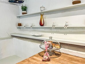 A kitchen with white walls, a wooden countertop, and a glass cake stand with pink decorations.
