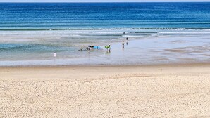 Una playa con gente caminando y llevando tablas de surf.