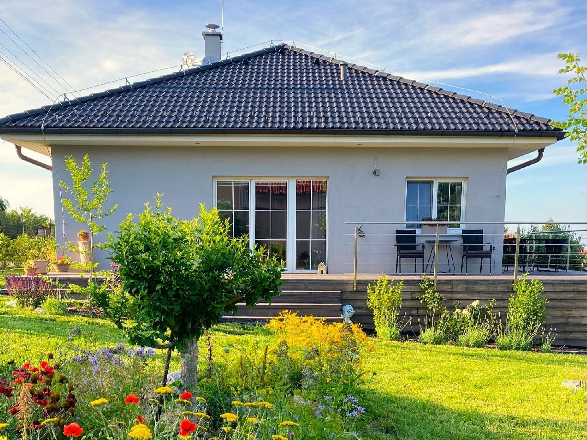 Une maison moderne avec un toit en tuiles, de grandes fenêtres et un jardin bien entretenu, agrémenté de diverses plantes et fleurs.