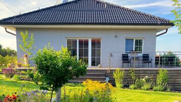 Une maison moderne avec un toit en tuiles, de grandes fenêtres et un jardin bien entretenu, agrémenté de diverses plantes et fleurs.