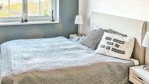 Un dormitorio con cama, una mesita de noche, una lámpara, una ventana y una lámpara colgante.