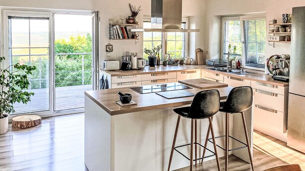 Cocina moderna con una isla grande, taburetes de bar y vistas al exterior.