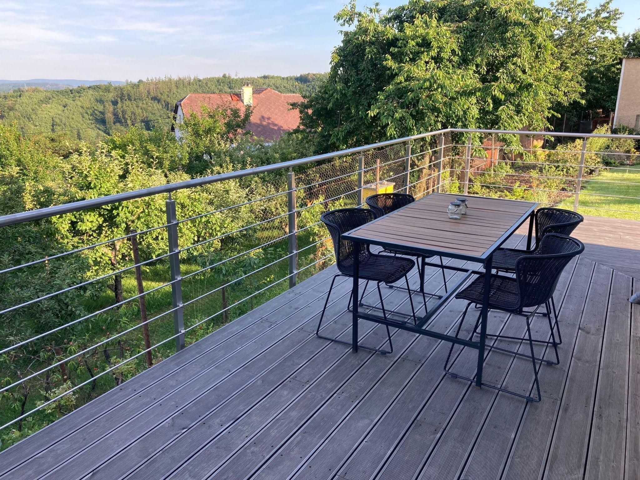 Une terrasse avec une table et des chaises, donnant sur une zone boisée.