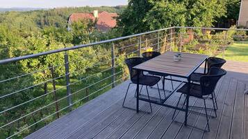Une terrasse avec une table et des chaises, donnant sur une zone boisée.