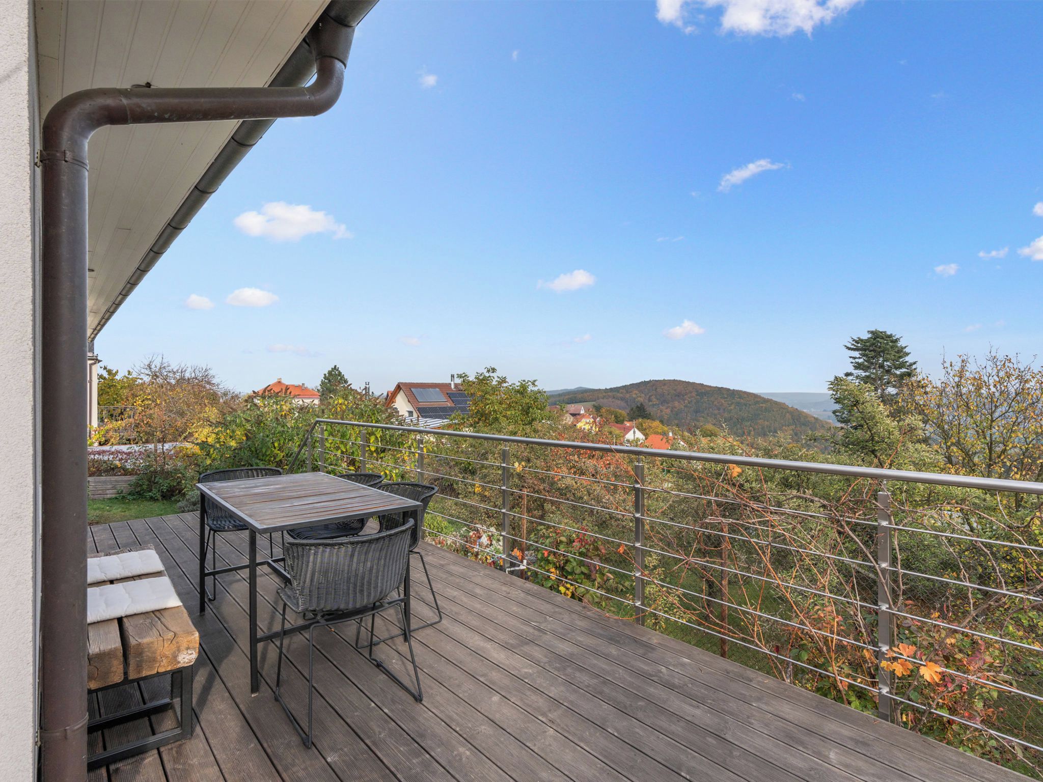 Eine Holzterrasse mit Tisch und Stühlen, mit Blick auf eine gebirgige Landschaft mit Häusern.