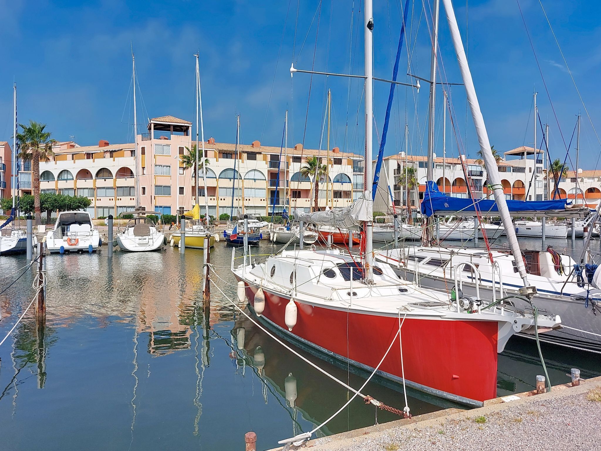 Un port de plaisance avec des bateaux amarrés, un bâtiment orné d’arches et un ciel dégagé.