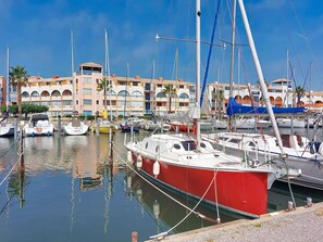 A marina with boats docked, a building with arches, and a clear sky. - Le Lamparo by Interhome (Port Leucate)