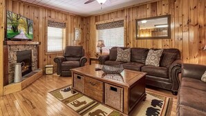 Ein Zimmer mit Holzwänden, einem Kamin, Ledersofas, einem Couchtisch und einem Deckenventilator.
