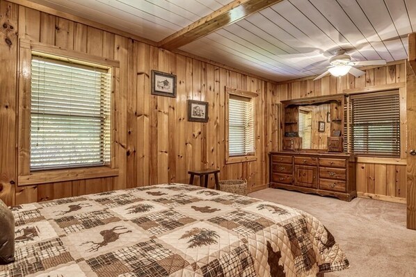 Een slaapkamer met houten lambrisering, een bed, een dressoir en een plafondventilator.