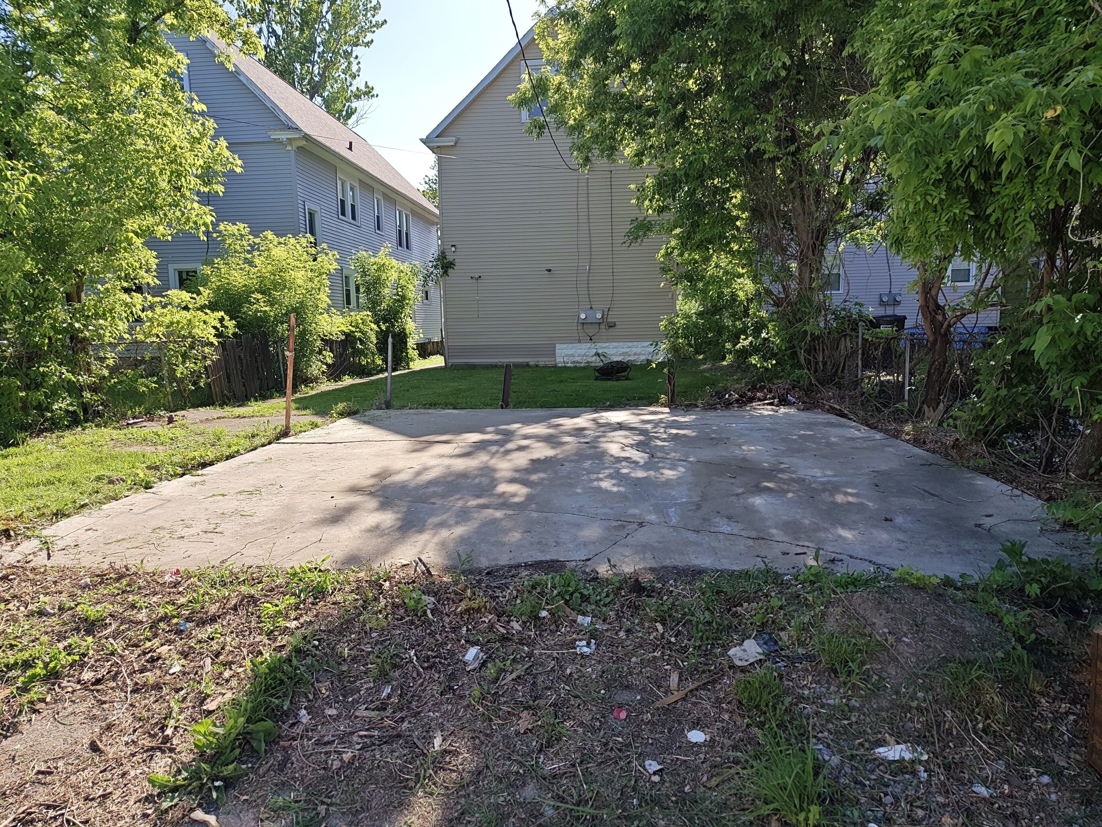 A residential driveway with a concrete surface, surrounded by grass and trees, leading to a house with a beige exterior.