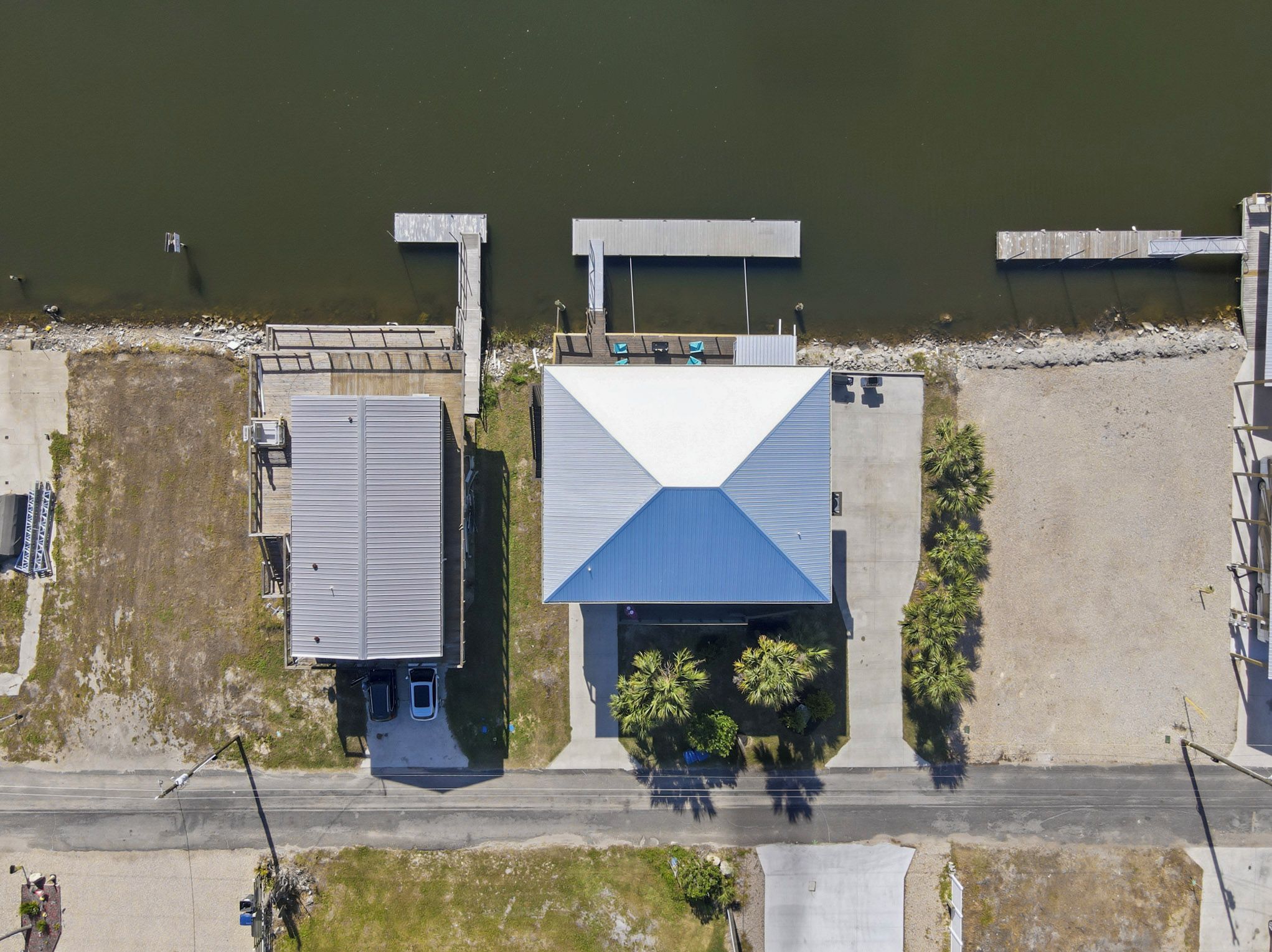 Une vue aérienne d’une propriété comprenant un grand bâtiment doté d’un toit bleu bien visible, une construction plus petite attenante et une jetée s’étendant dans une étendue d’eau.
