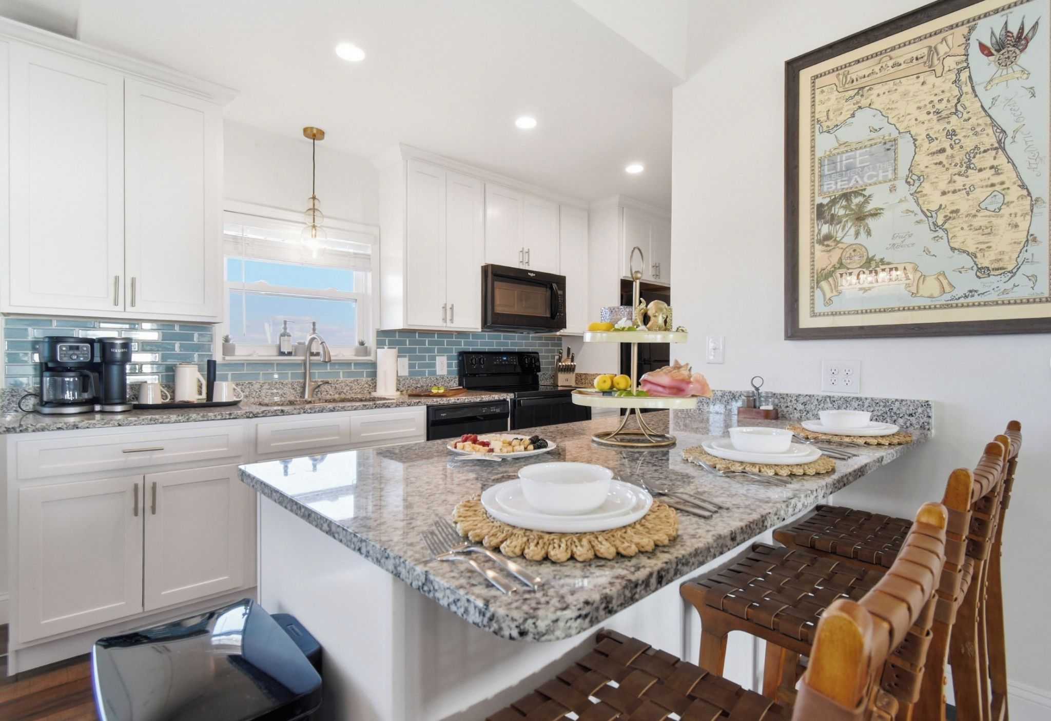 A modern kitchen with white cabinets, a granite countertop, and a dining area with a map on the wall.