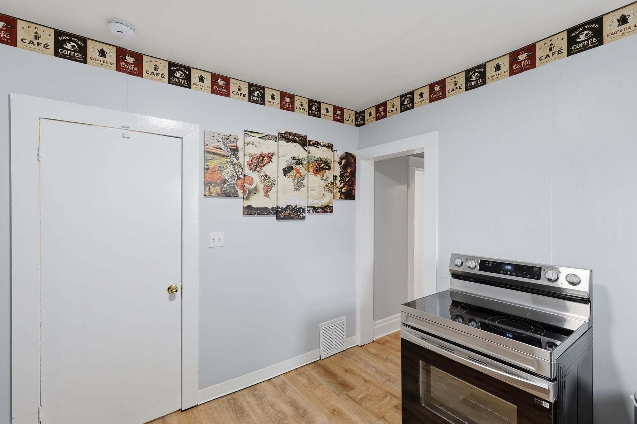 A kitchen with a stainless steel oven, a white door, and a wall with a coffee-themed border.