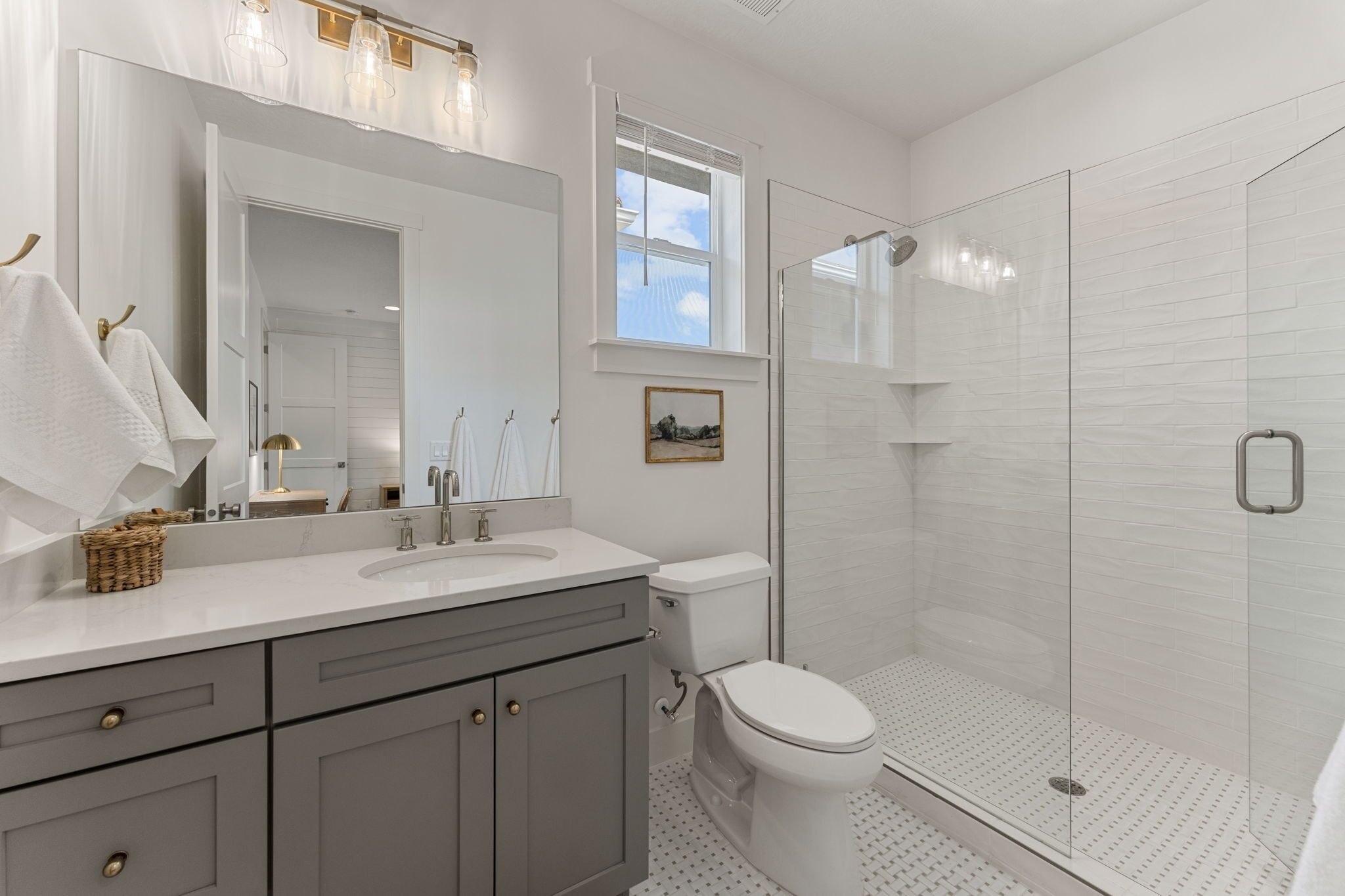 A modern bathroom with a large mirror, white fixtures, a shower enclosure, and a window.