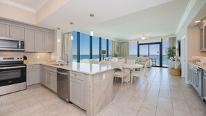 A modern kitchen with a large island, a dining area with a view, and a living space with a balcony overlooking the ocean. - Phoenix Gulf Shores Ii 405 4 Bedroom Condo (Gulf Shores)
