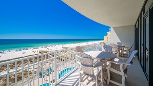 A balcony with a view of a beach and ocean, white chairs, and a table. - Phoenix Gulf Shores Ii 405 4 Bedroom Condo (Gulf Shores)