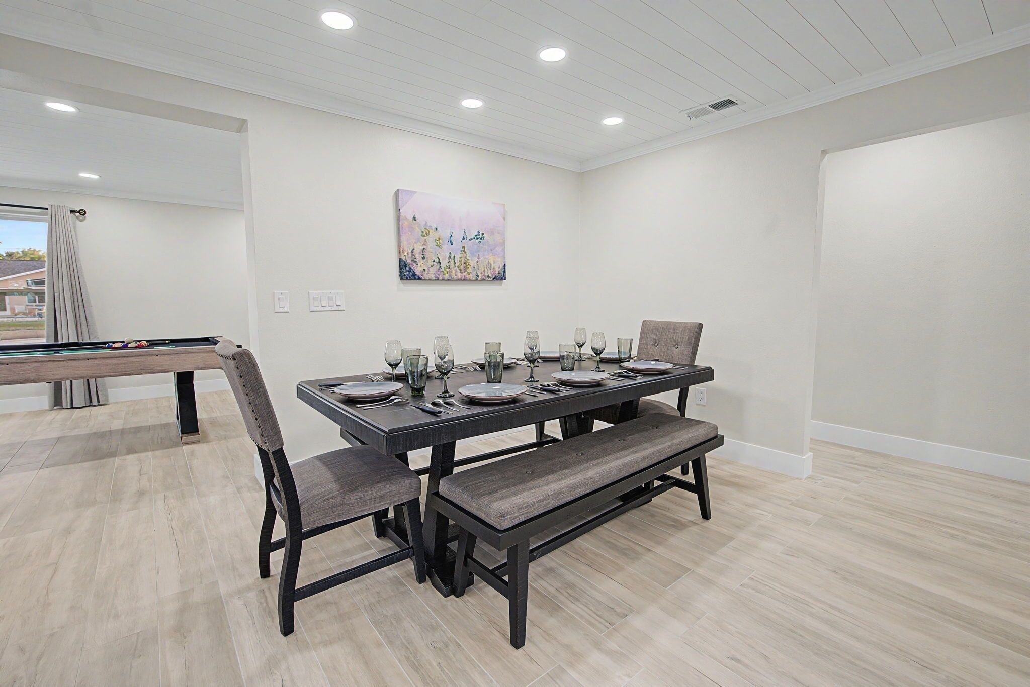 A dining area with a pool table, a long table with benches, and a painting on the wall.