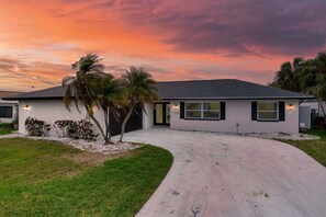 A single-story house with a driveway, palm trees, and a sunset sky. - Harbor Island - 4900 Shoreview Ct 3 Bedroom Home (Port Richey)