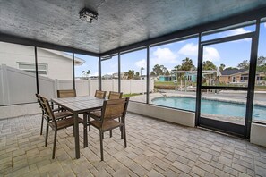 Un patio techado con piscina, una mesa con sillas y vistas a casas vecinas.