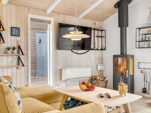 A cozy living room with a TV, fireplace, wooden walls, and a dining area with a fruit bowl.
