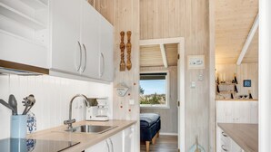 Eine moderne Küche mit weißen Schränken, einer Kaffeemaschine und Blick in ein Schlafzimmer mit Bett und Fenster.