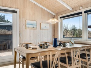 A wooden interior with a dining table, chairs, artwork, and a window with a view.