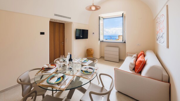 Uma sala de jantar com mesa de vidro, cadeiras e um sofá com vista para o mar.
