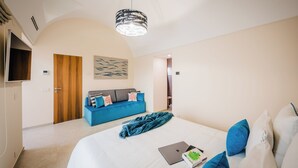 Um quarto com uma cama, um sofá azul, uma porta de madeira e uma televisão fixada na parede.