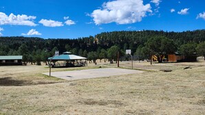 Un campo abierto con un pabellón, una cancha de baloncesto y una colina boscosa al fondo.