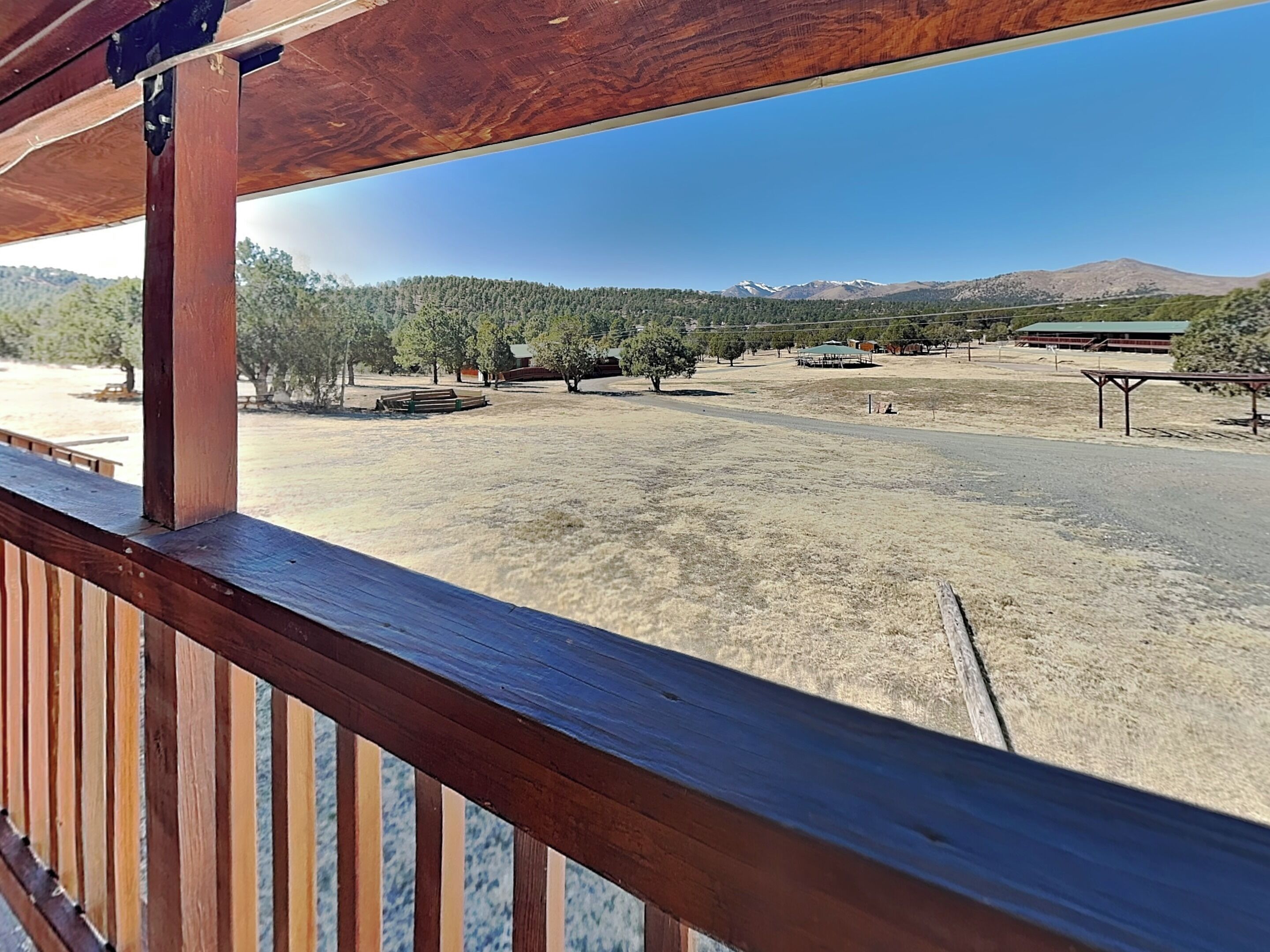 Ein hölzerner Balkon mit Blick auf eine trockene, offene Landschaft mit Bäumen und fernen Bergen.