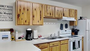 A kitchen with wooden cabinets, a white countertop, a stove, and a refrigerator. - Pine Lodge Cabin: Spacious + Mountain Views (Alto)