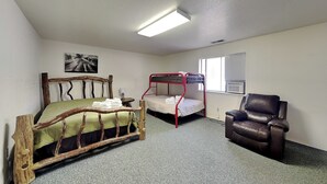 A room with a wooden bed, a bunk bed, a leather chair, and a window with blinds. - Pine Lodge Cabin: Spacious + Mountain Views (Alto)