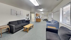 A living room with a sofa, a coffee table, a TV, and a kitchen area in the background. - Pine Lodge Cabin: Spacious + Mountain Views (Alto)