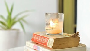 Una pila de libros con una vela encima, sobre una superficie reflectante.