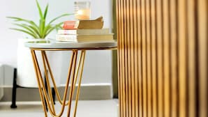 Una mesa pequeña con libros, una vela, una planta en maceta y un muro de listones de madera.