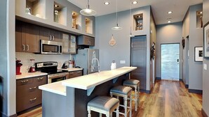 A modern kitchen with a central island, bar stools, and pendant lighting. - Ocean Grove PH 1101 | Stunning Penthouse & Gulf Views! (Galveston)