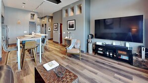 A modern living room with a dining area, a large flat-screen TV, and a wooden coffee table. - Ocean Grove PH 1101 | Stunning Penthouse & Gulf Views! (Galveston)