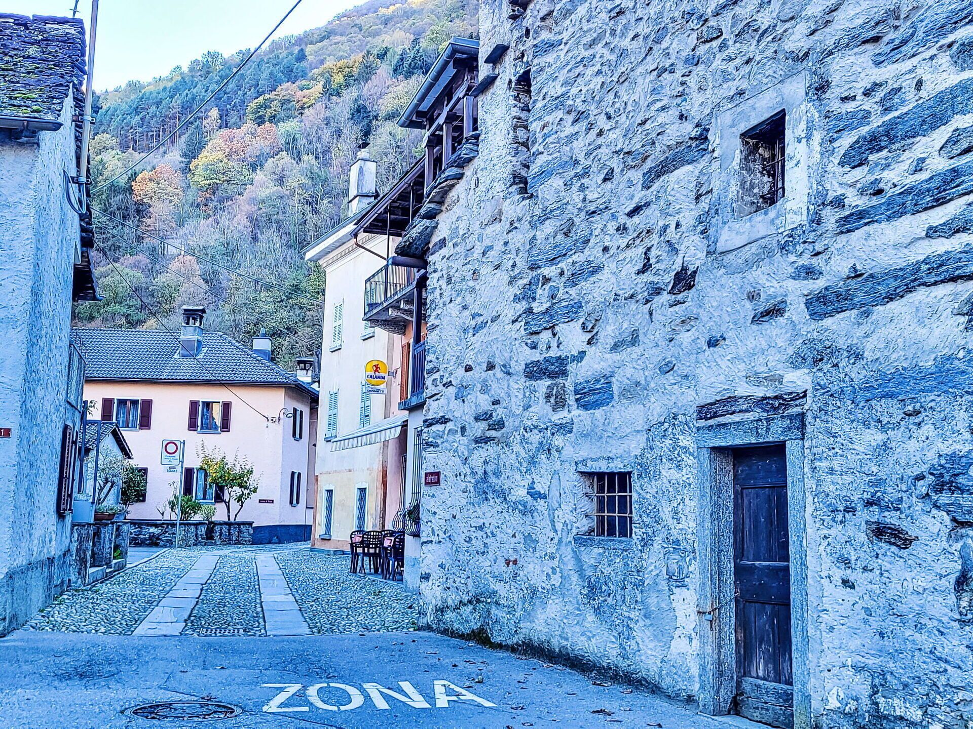 Une rue étroite bordée d’immeubles en pierre, avec une signalisation bien visible indiquant une « ZONE », et un immeuble doté d’un balcon.