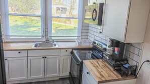 A kitchen with white cabinets, a stainless steel sink, a wooden countertop, and a black stove. - Modern 1 BR Near York - Sleeps 3 - Renovated (Hallam)