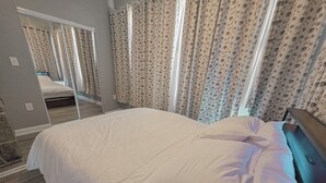 A bedroom with a large bed, a mirror, floral curtains, and a wooden floor. - Modern 1 BR Near York - Sleeps 3 - Renovated (Hallam)