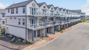 A row of modern, multi-story residential buildings with balconies, a paved driveway, and a clear sky. - Eazy Breezy: Ocean Views, Dog-Friendly Rockaway Beach Townhome for 8 (Rockaway Beach)