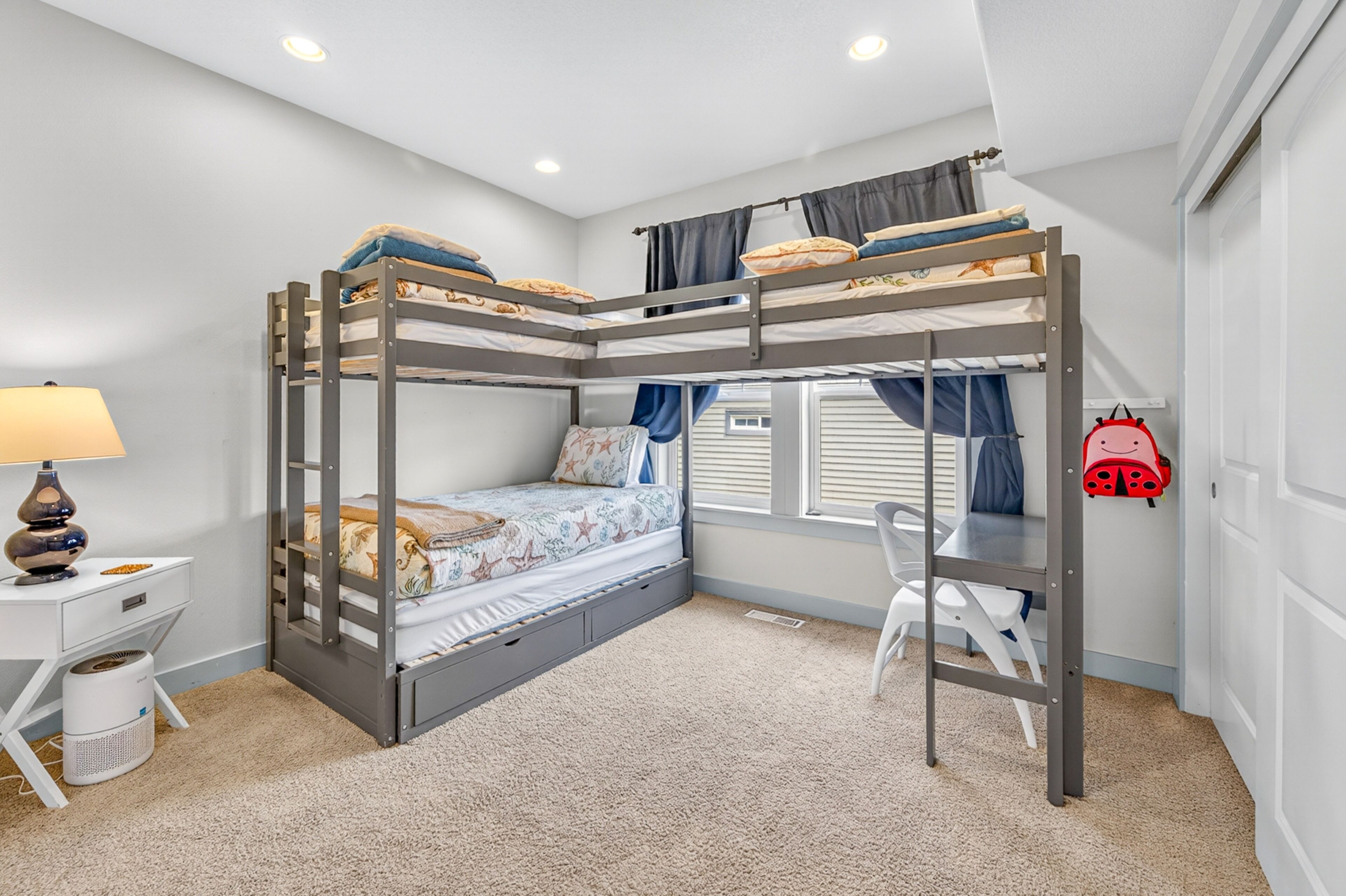 A bunk bed room with a desk, chair, lamp, and a red backpack.